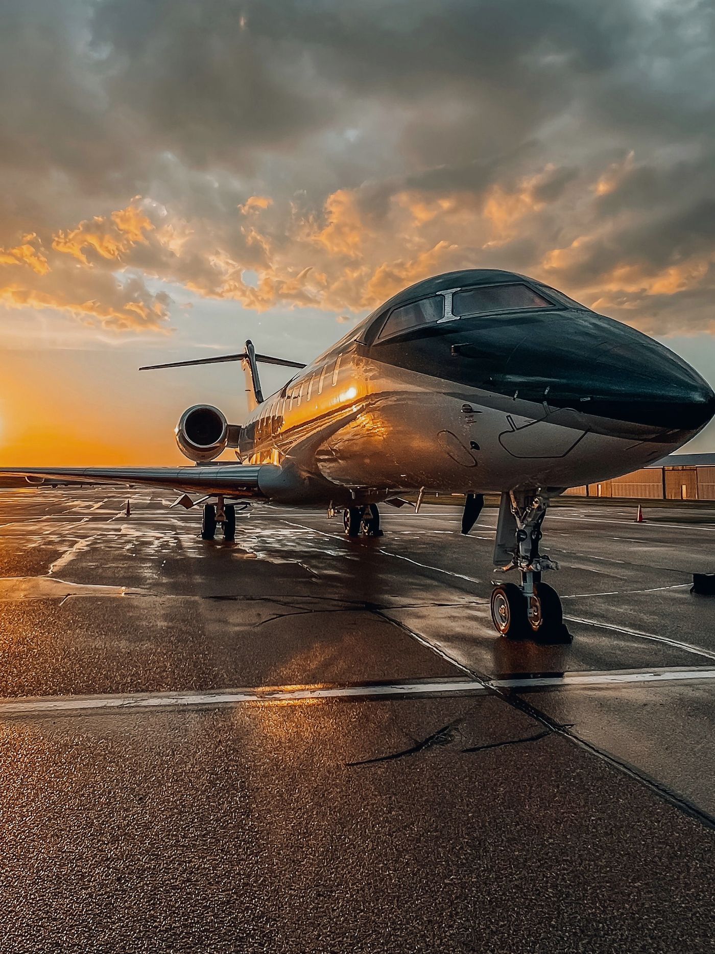 Business jet on a rain-wet ramp under a golden sunset sky