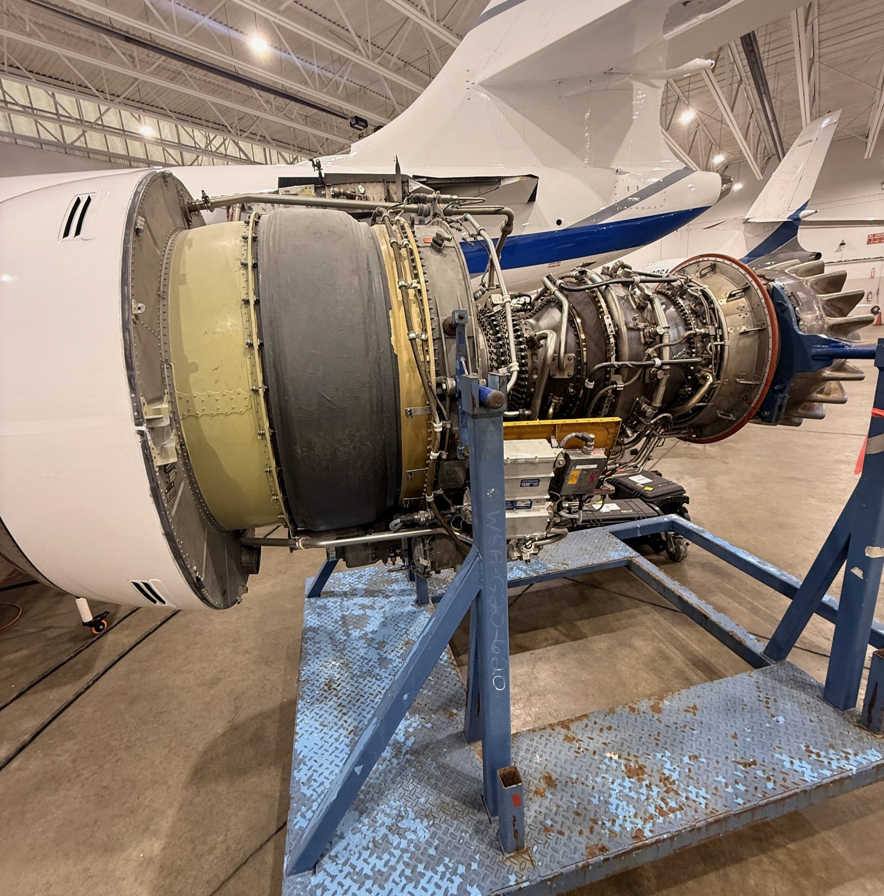 Business jet turbofan engine off-wing on a blue engine stand in a hangar